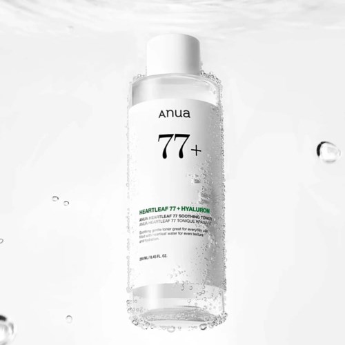 Tydlig flaska med vit lock, märkt anua 77+ Heartleaf och Hyaluron, omgiven av vattendroppar.