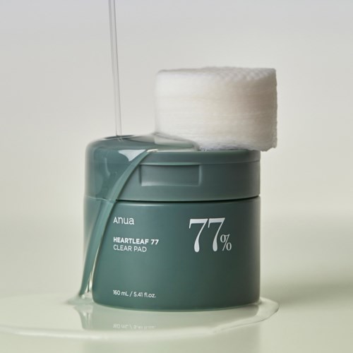 En teal behållare med Anua Heartleaf 77 Clear Pads, en bomullstuss på toppen och vätska som rinner ut.