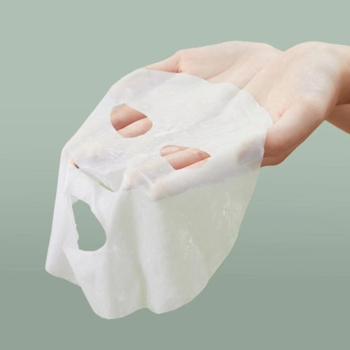 Eine Hand hält eine Gesichtsmasken aus Papier, die so geformt ist, dass sie das Gesicht mit Löchern für Augen, Nase und Mund bedeckt.
