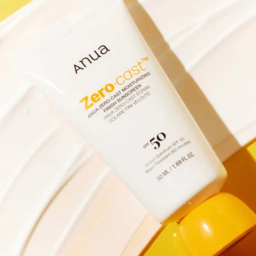 En hvid flaske med Anua Zero-Cast SPF 50 solcreme med gylden hætte, hvilende mod en hvid væg.