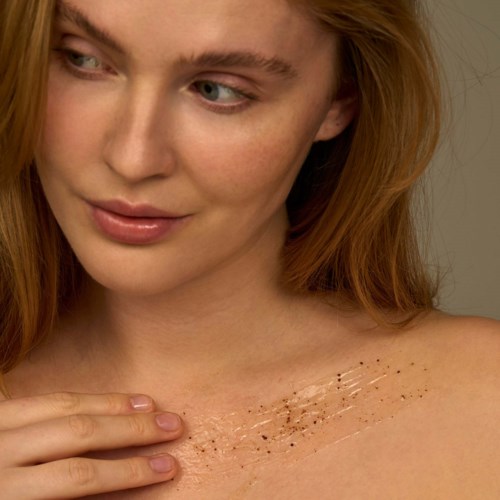A woman shows her shoulder with some small glittery makeup or tattoo. She looks gently at her shoulder.