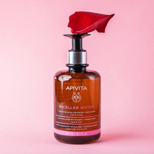 Een bruin flesje met 'APIVITA Micellar Water' en een rozenblad op de dop, tegen een roze achtergrond.