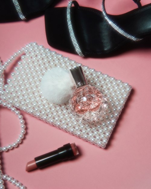 Juveler, läppstift och ett pärlhalsband på en rosa bakgrund med en svart sko i närheten.