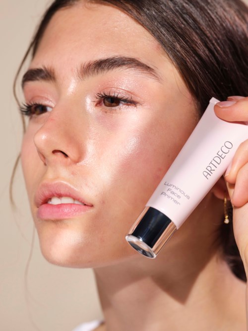 En kvinde påfører et hudplejeprodukt på ansigtet, holder et rør mærket 'ARTDECO Luxury Face Primer'.