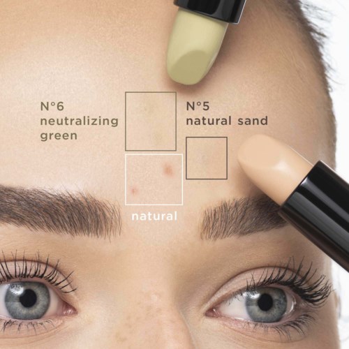 En person bruger concealer i forskellige nuancer på panden og omkring øjenbrynene, mærket som naturlig, grøn og sand.