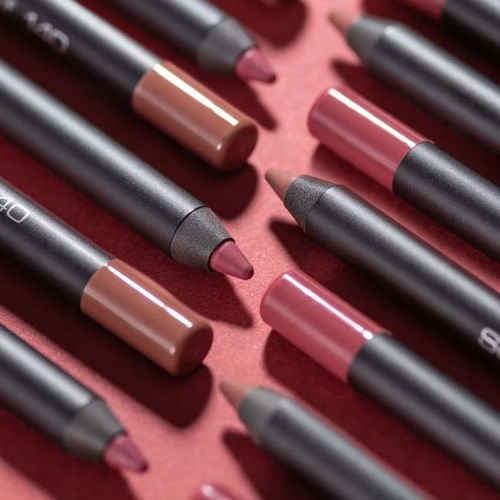Multiple lip crayons in various shades arranged on a pink background.