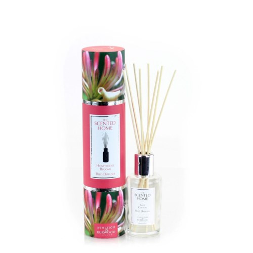 En duftspreder med rosa blomsterlabel og pinde i en gennemsigtig flaske, ved siden af en matchende cylindrisk kasse.