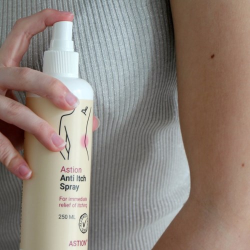 Osoba trzyma białą butelkę z sprayem oznaczoną "Astion Anti Itch Spray" obok ramienia.