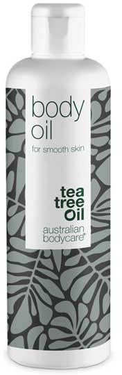En vit flaska med svarta och grå bladmönster, märkt som kroppsolja med tea tree-olja, för slät hud.