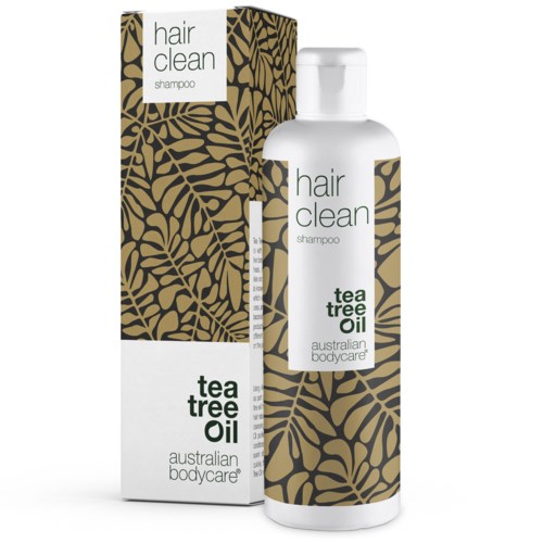 A white shampoo bottle with a matching box, featuring black and gold leaf design and text about tea tree oil.