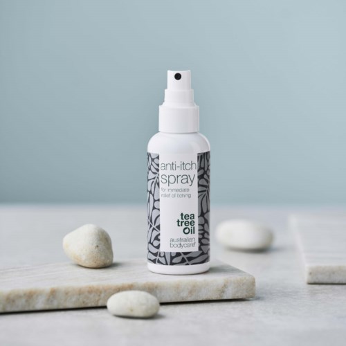 En liten hvit sprayflaske merket 'anti-itch spray' med tea tree oil, plassert på en steinflate med små steiner.