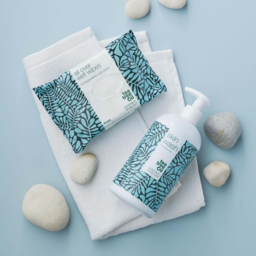 Skincare products with blue leaf patterns, including wet wipes and skin wash, on a white towel with stones around.