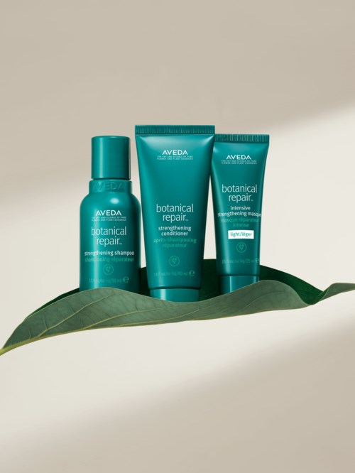 Tre blågrønne flasker og rør med Aveda Botanical Repair-hårpleieprodukter på et blad.
