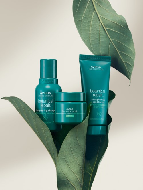 Tre grønne hårpleieprodukter blant grønne blader, merket som Aveda Botanical Repair. De inkluderer sjampo, balsam og behandling.