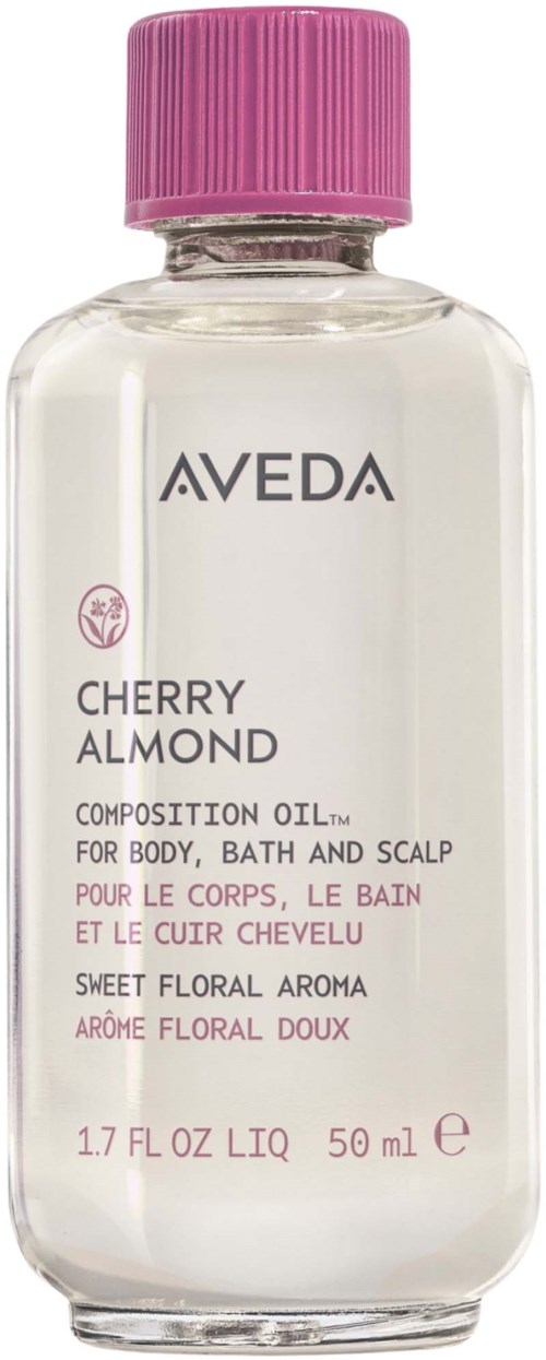 En gjennomsiktig flaske med Aveda Cherry Almond kroppsolje med rosa kork og hvit etikett som viser produktdetaljer.