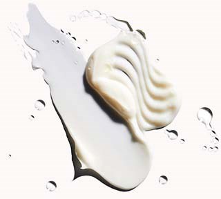 En vit, kurvig klick av grädde eller lotion på en vit yta med spridda droppar runt omkring.