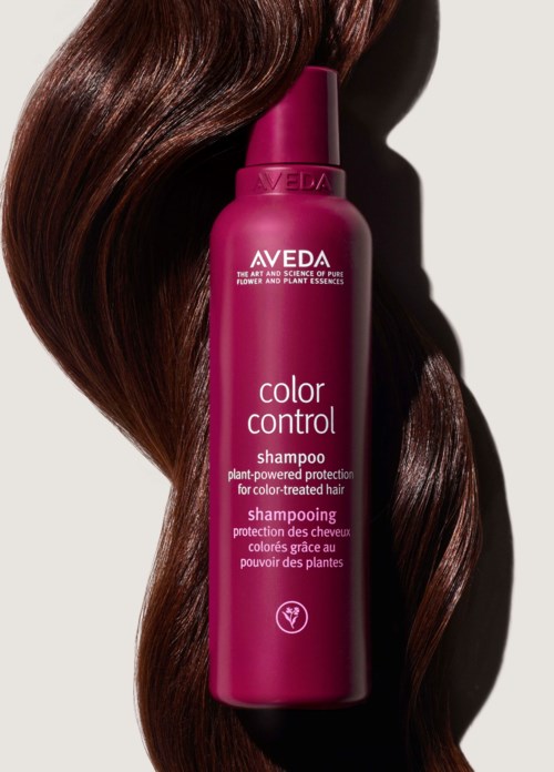 En rosa flaske av Aveda Color Control Shampoo med blank brunt hår ved siden av.
