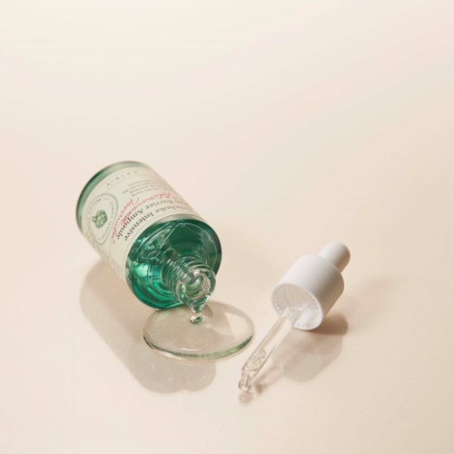 A bottle of liquid, dropper, and a small glass dish on a plain surface.
