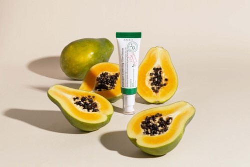 Tre papaya-halv deler og en hel papaya sammen med et rør med hudpleieprodukter på en nøytral bakgrunn.