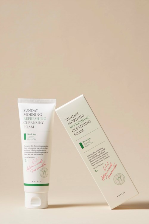 A white tube of facial cleansing foam and its box stand against a beige background.
