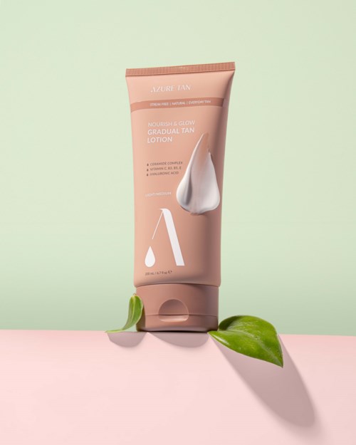 A pink tube of lotion with a leaf in front, on a two-tone background, promoting gradual tan and glow.