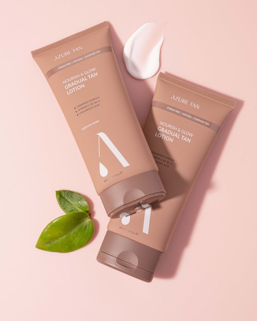 Two beige tubes of lotion are placed on a pink background, with a green leaf and a dollop of cream.