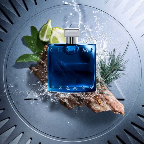 Błękitna butelka perfum z napisem 'Chrome' na kamieniu, obok plastry limonki, gałązka sosny i rozbryzgi wody.