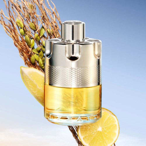 Butelka perfum z metalową zakrętką, otoczona plastrami cytryny i rośliną na niebieskim tle.