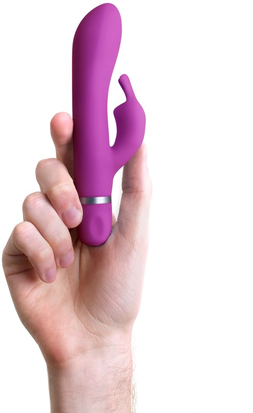 En hand håller ett lila, kurvat vuxenleksak robot med ett litet finger. Bakgrunden är renvitt.