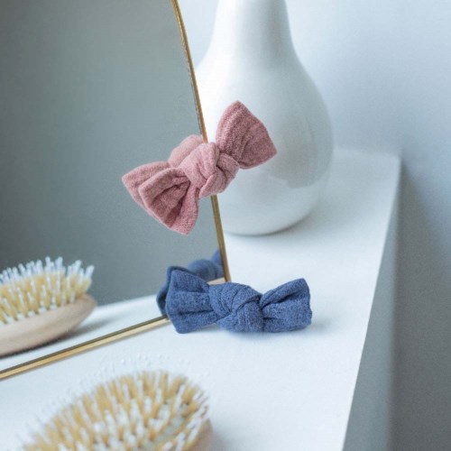 Zwei Stoffschleifen, eine rosa und eine blaue, sind an einem Spiegel befestigt und auf einer weißen Oberfläche platziert.