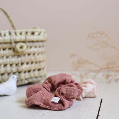 Weiche Stoff-Schlaufen in Rosa und Beige liegen auf einer weißen Oberfläche mit Korb und Dekorationspflanze im Hintergrund.