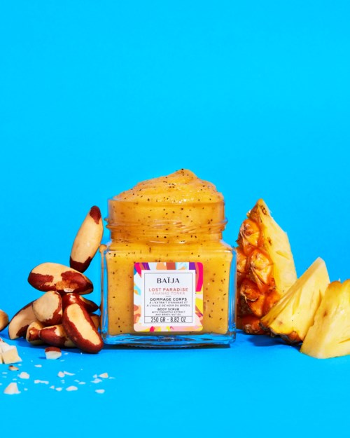 Żółty pojemnik na peeling do ciała z tropikalnymi owocami wokół na niebieskim tle.