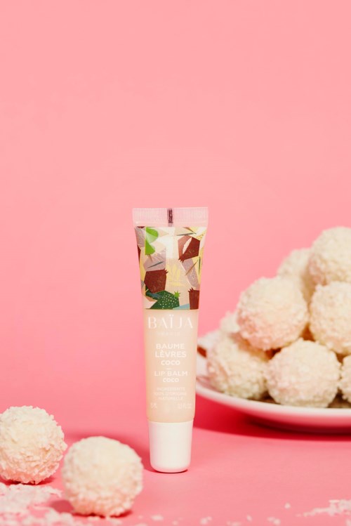 Eine Tube Hautcreme steht auf pinkem Hintergrund mit weißen flauschigen Kugeln in der Nähe.