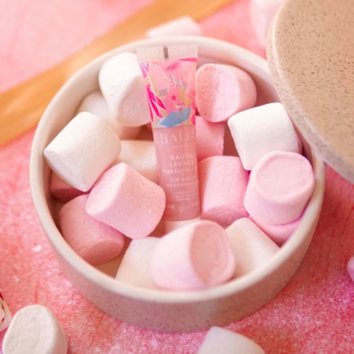 A small tube of lip balm surrounded by pink and white marshmallows on a pink background.