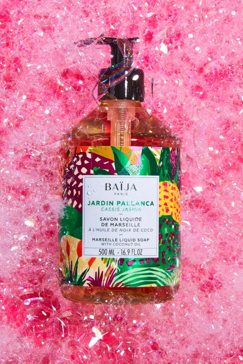 Färggalld tvålflaska med tropiska blad och blomster på rosa bakgrund.