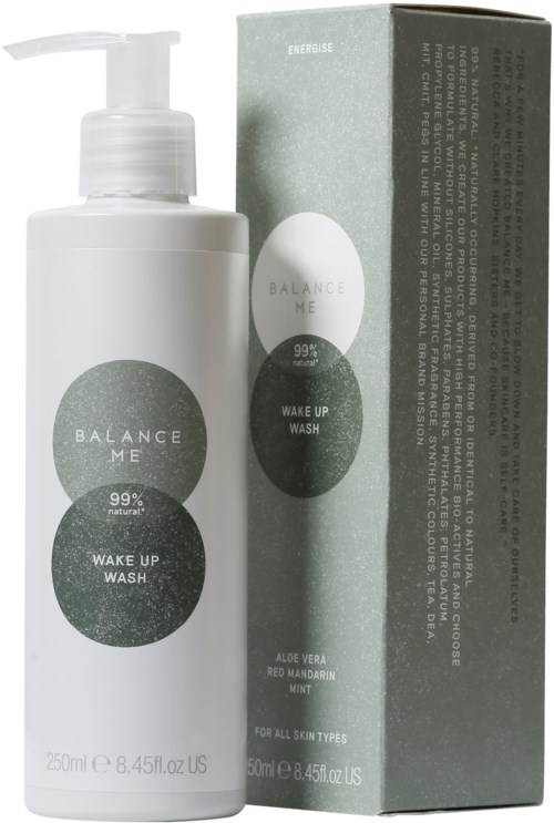 En vit flaska med pump bredvid en förpackning, båda märkt 'Balance Me Wake Up Wash' med naturliga ingredienser.