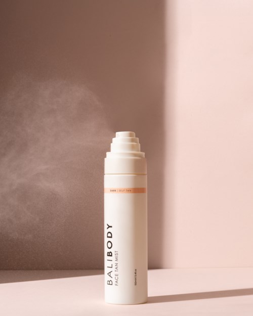 En vit sprayflaska märkt 'BODY' sprutar dimma i luften mot en tvåfärgad bakgrund.