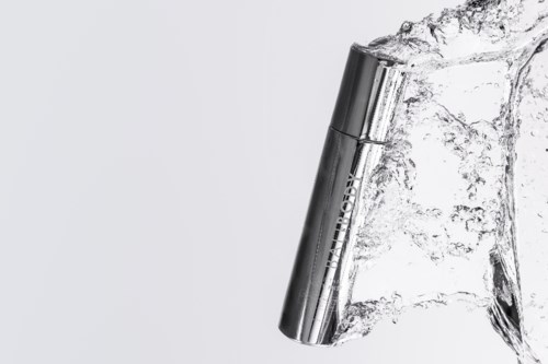 Ein silbernes zylindrisches Gerät, das mit Wasser spritzt, mit metallischem Finish, vor einfachem Hintergrund.