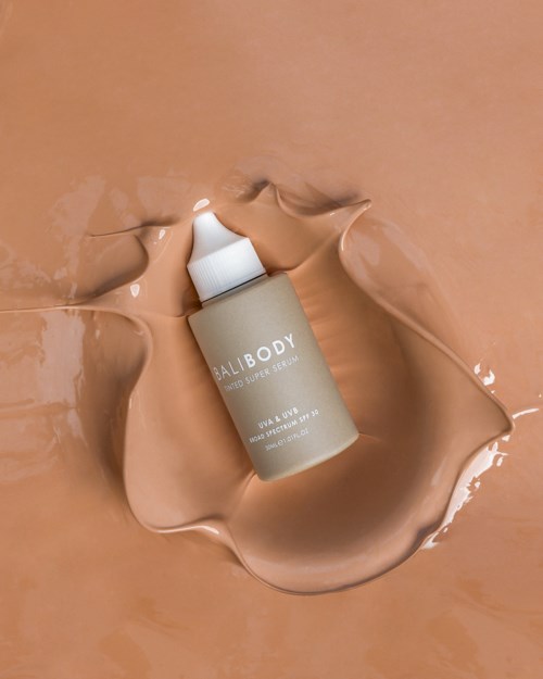 Eine Flasche mit der Aufschrift 'BALIBODY', umgeben von geschmolzener beiger Creme auf einer flachen Oberfläche.