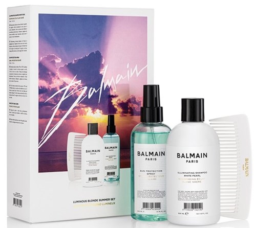 Ett Balmain hårvårdsset med schampo, spray, läppstift och kam, med en färgglad solnedgång i bakgrunden och rosa signatur.