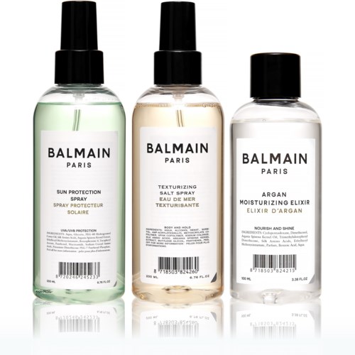 Three bottles of Balmain skincare products with black caps, each labeled for different uses: sun protection, salt spray, and moisturizer.