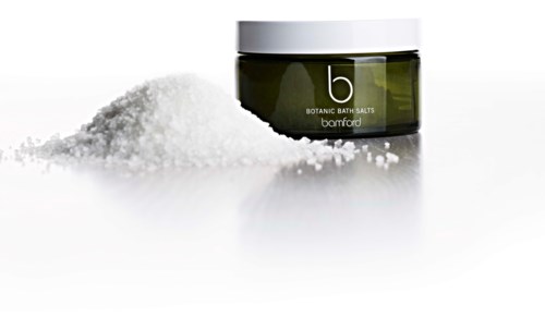 En mörkgrön burk med badsalt bredvid en hög av salt, märkt 'b' och 'Botanic Bath Salts Bamford.'