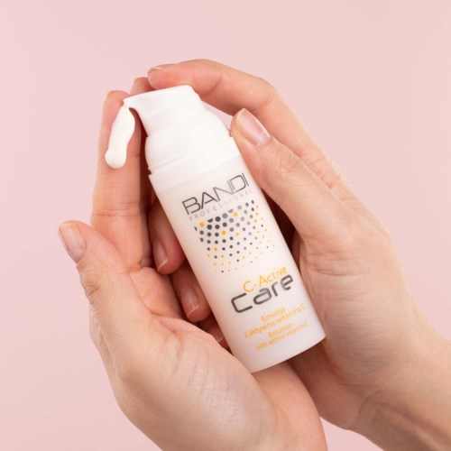 En hand håller en vit flaska med pump som är märkt 'Active Care' och 'Bandi' mot rosa bakgrund.