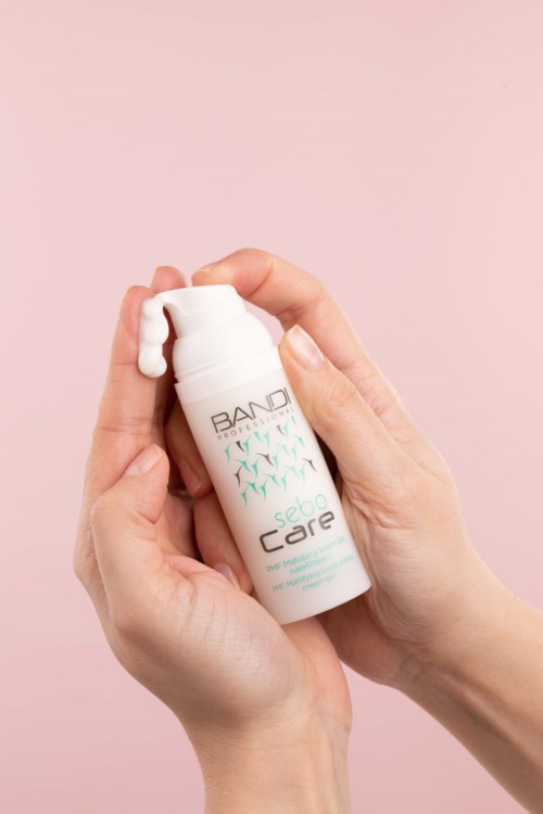 A person holds a white bottle labeled 'SEBIA Care' with a small dollop of white cream on top.