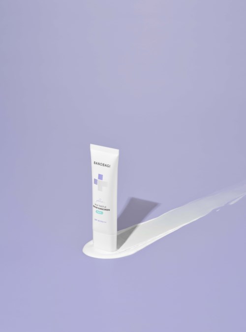 A tube of skincare cream standing on a purple surface, with cream spilling out. The tube has text and a purple design.