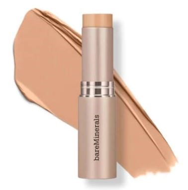 A beige stick of makeup cream with a silver band, lying on a beige swatch. The brand name is BareMinerals.