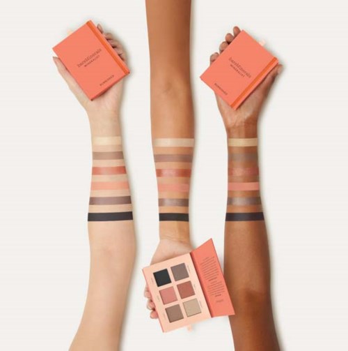 Three arms show various makeup swatches and pink makeup product boxes, with one arm holding an eyeshadow palette.