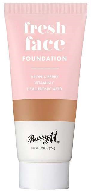 En rosa tube med foundation med hvit og svart tekst, sier den inneholder aroniabær, vitamin C og hyaluronsyre.