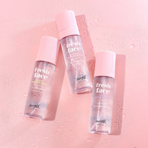 Tre små flaskor med setting spray på en rosa yta med vattendroppar.