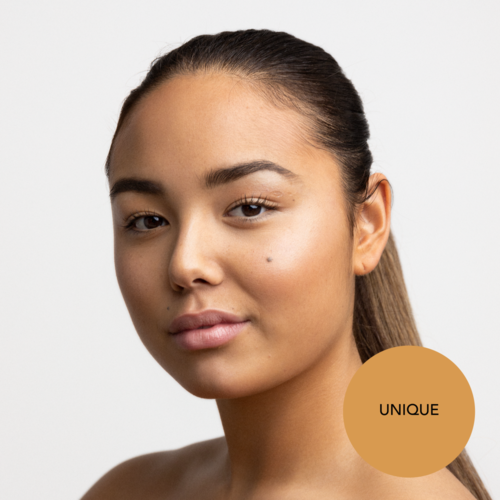 En kvinna med slät hud och ett självsäkert uttryck, utan synlig makeup, med en guldstämpel som säger 'UNIQUE'.